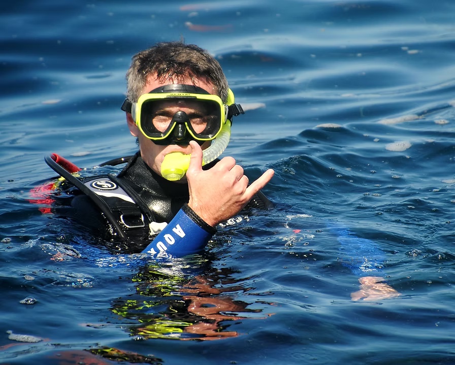 Tim Gubler scuba diving, wearing a mask and giving a hand gesture at the water’s surface
